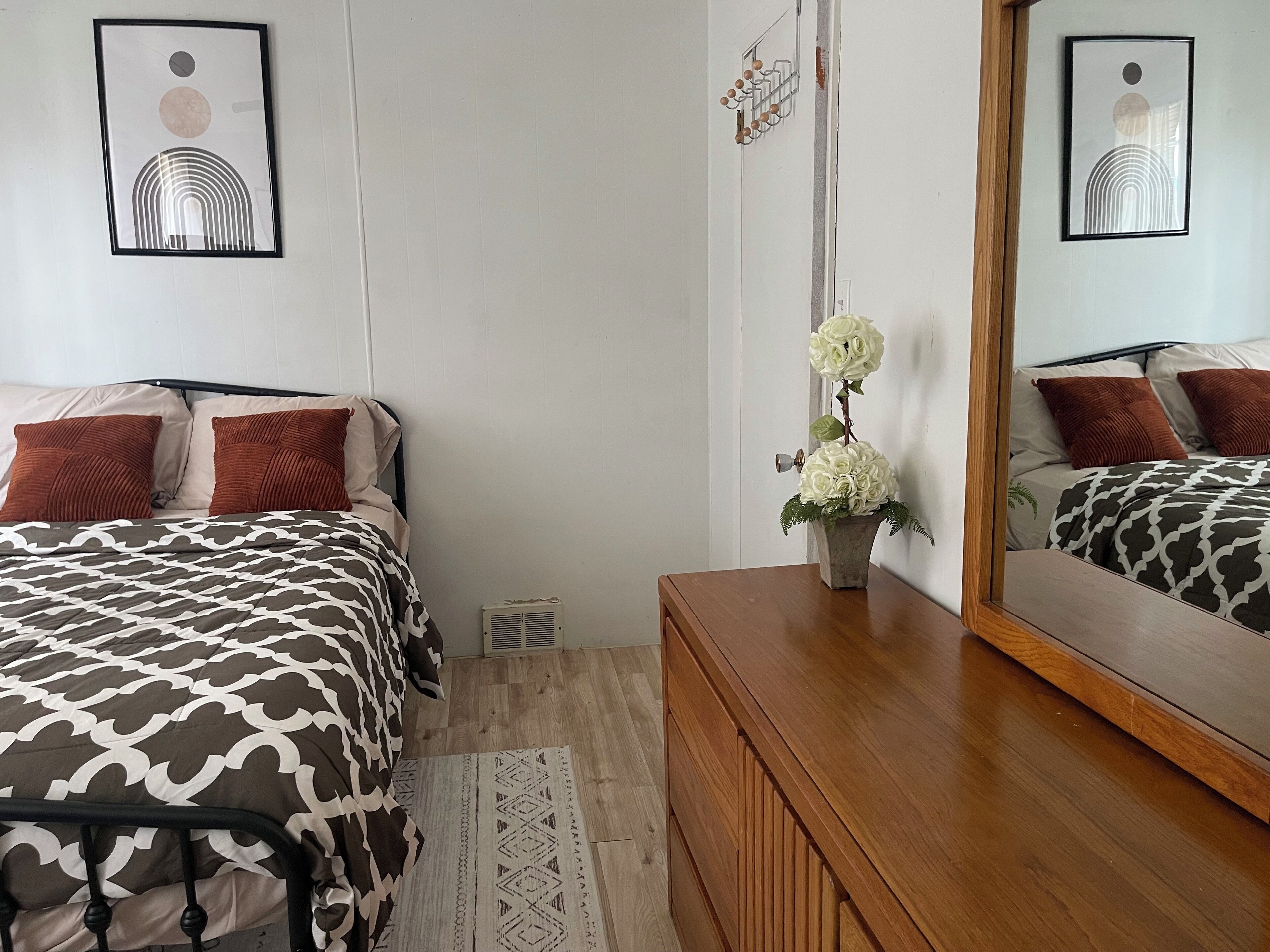 A bedroom with a bed, a dresser, a mirror, and a wall-mounted air vent.