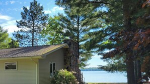 Une petite cabane avec une cheminée en pierre, entourée d’arbres et bordée par un lac.