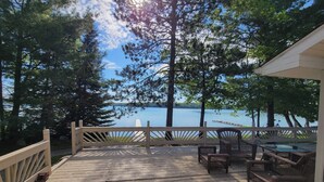 Une terrasse en bois, agréée de mobilier d’extérieur, qui offre une vue sur un lac bordé d’arbres et sur un ciel dégagé.
