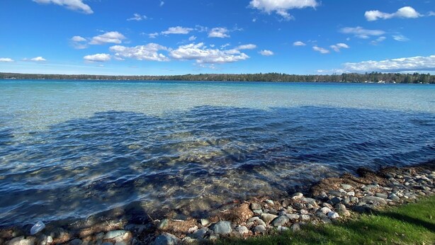 Un lac aux eaux limpides, avec des rochers visibles sur la rive et une ligne d’arbres à l’horizon.