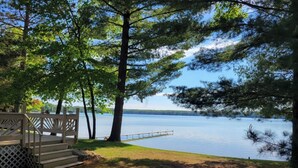 Une terrasse au bord du lac, avec des marches menant à un quai, entourée d’arbres et offrant une vue dégagée sur le lac.
