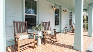 Eine Veranda mit zwei Holzstühlen, einem Tisch, einem Blumentopf und einem Hausnummernschild.