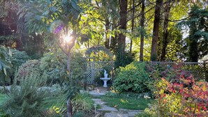 A garden pathway leading to a statue, surrounded by various plants and trees.