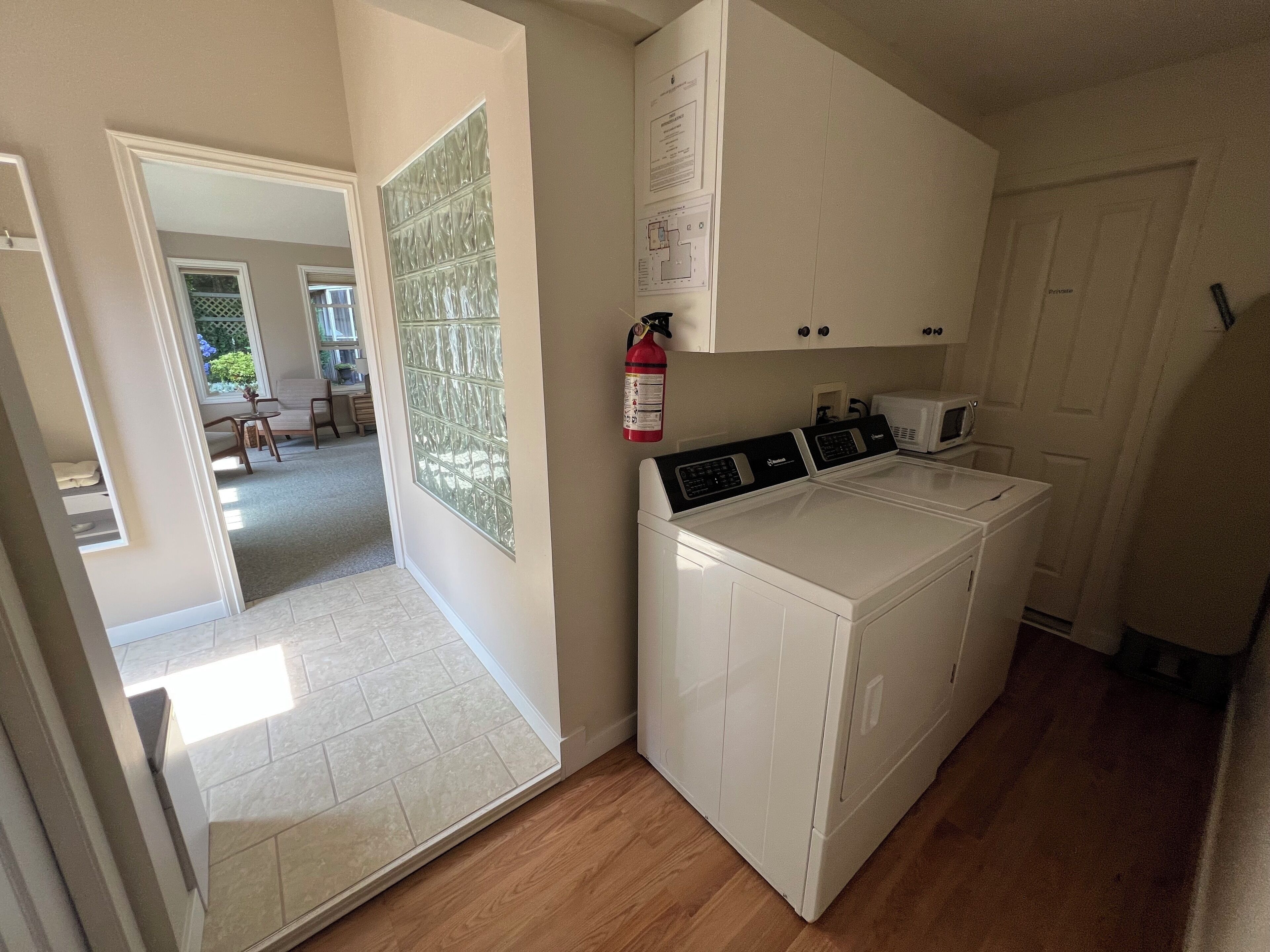 A laundry area with a front-loading washer and dryer, a fire extinguisher, and a door leading to a dining area.
