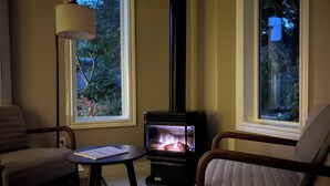 A cozy living room with a wood-burning stove, two armchairs, a small table, and a floor lamp.