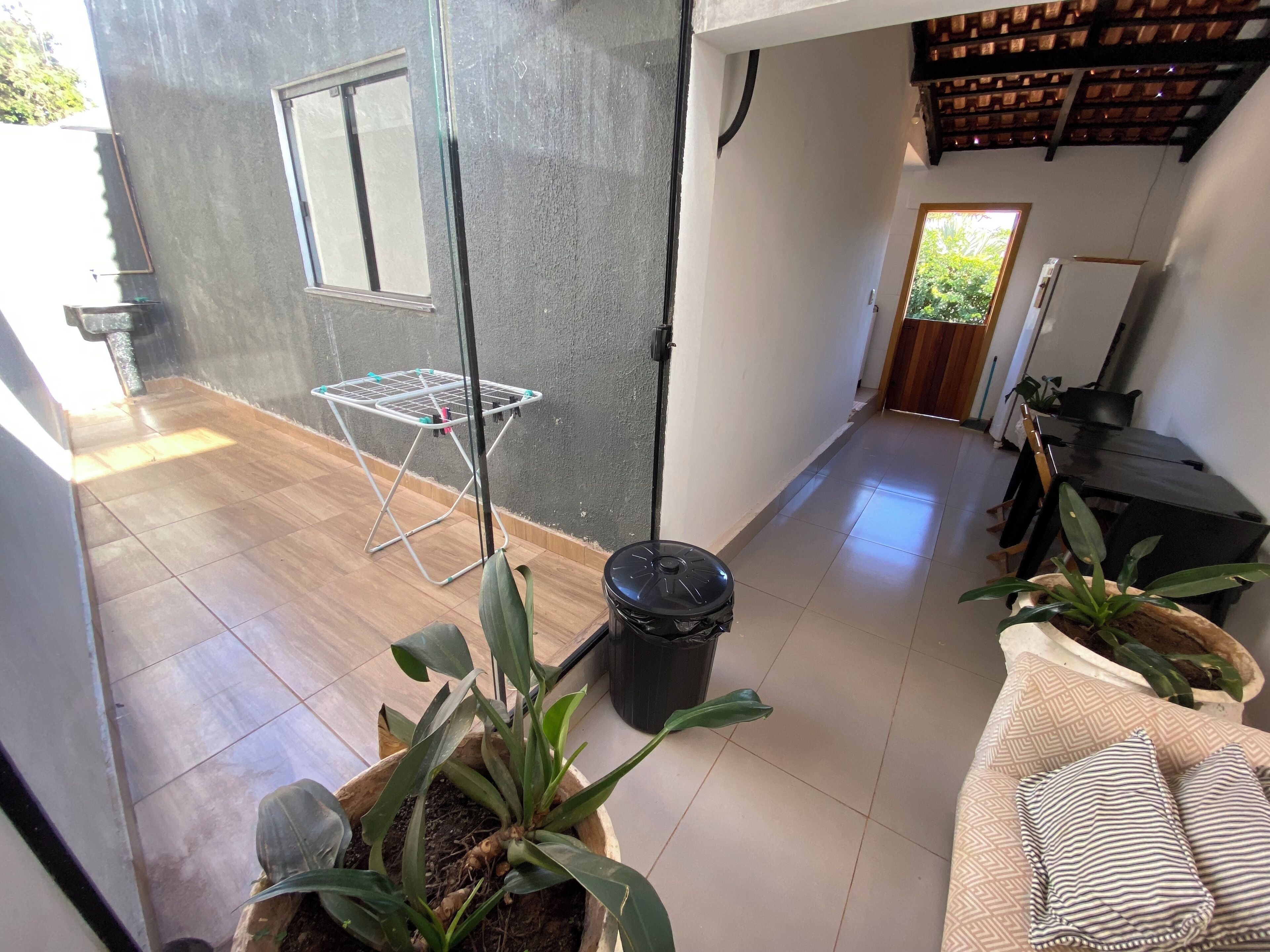 A modern interior with a tiled floor, a drying rack, potted plants, and a black table with a white appliance.
