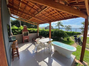 Une terrasse extérieure avec un barbecue, une table et des chaises, une baignoire blanche et une vue sur un lac et des palmiers.