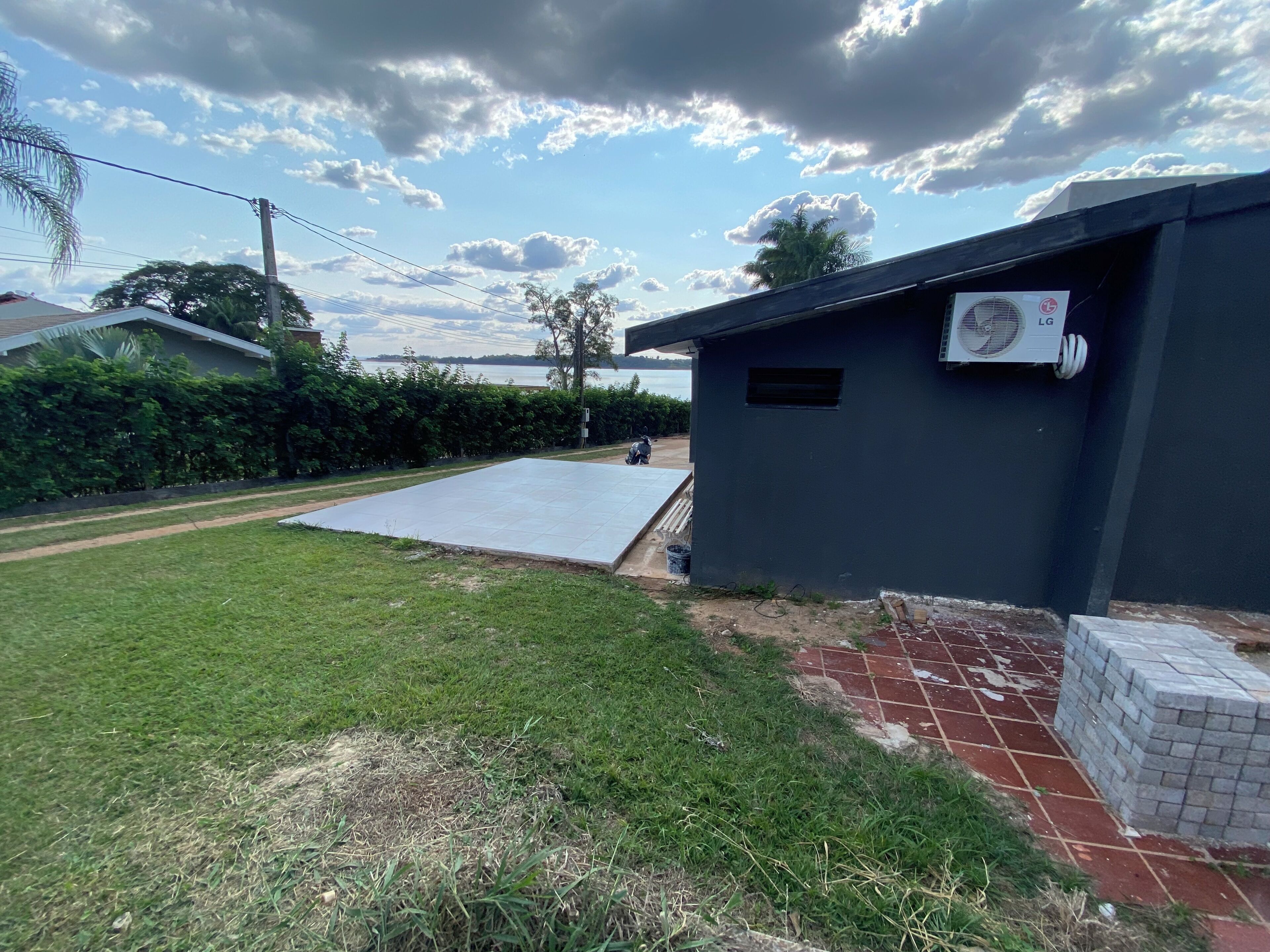 A residential area with a paved patio, a small shed with an air conditioning unit, and a grassy lawn.