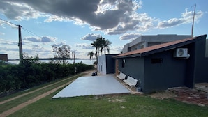 A modern building with a flat roof, a paved patio, and a view of the water. - Villa Querência (Avare)