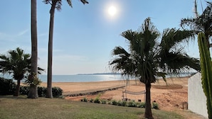 A beach view with palm trees, a hammock, and a white wall. - Villa Querência (Avare)
