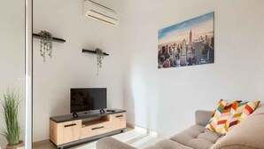 Un soggiorno moderno con una TV a schermo piatto su un mobile in legno, un divano e un cuscino colorato.