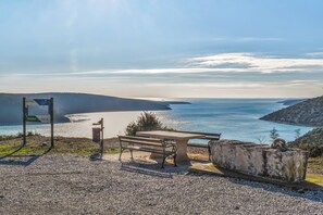 Eine Bank und ein Schild in Küstennähe mit Blick auf das Meer und die Hügel.
