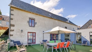 A building with a stone facade, a covered patio with outdoor seating, and a green lawn. - Le Paradis (Orcival)