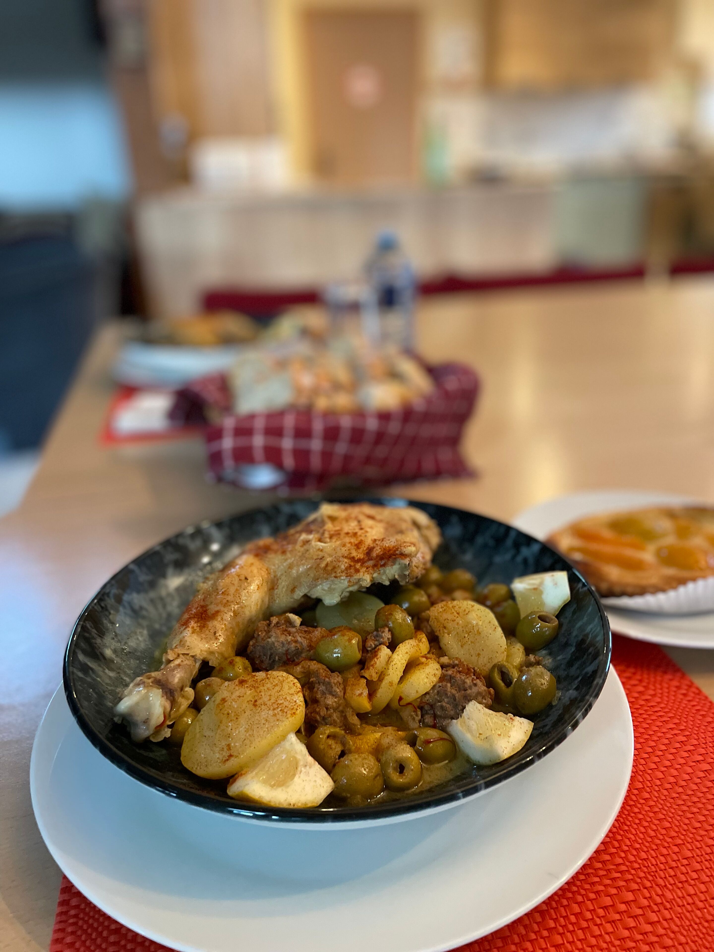En skål med mat innehållande kött, potatis och oliver, serverad på en tallrik.