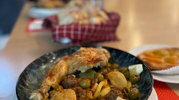 En skål med mat innehållande kött, potatis och oliver, serverad på en tallrik.