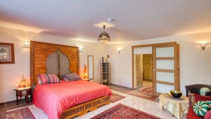 A bedroom with a bed, wooden headboard, bedside lamps, a small table with a bowl, and a chair. - Le Paradis (Orcival)