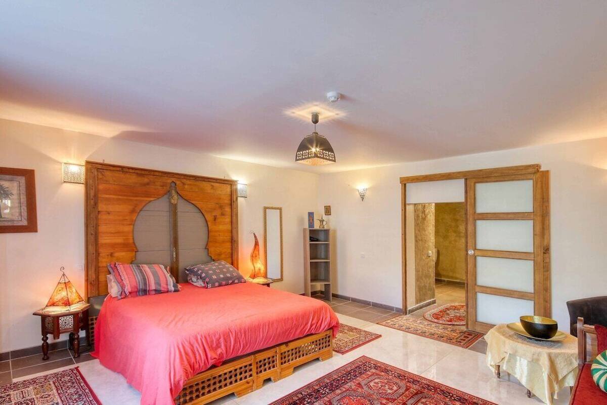 Une chambre à coucher avec un lit, une tête de lit en bois, des lampes de chevet, une petite table avec un bol et une chaise.