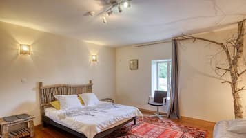 A bedroom with a bed, bedside table, lamp, chair, and a large window.