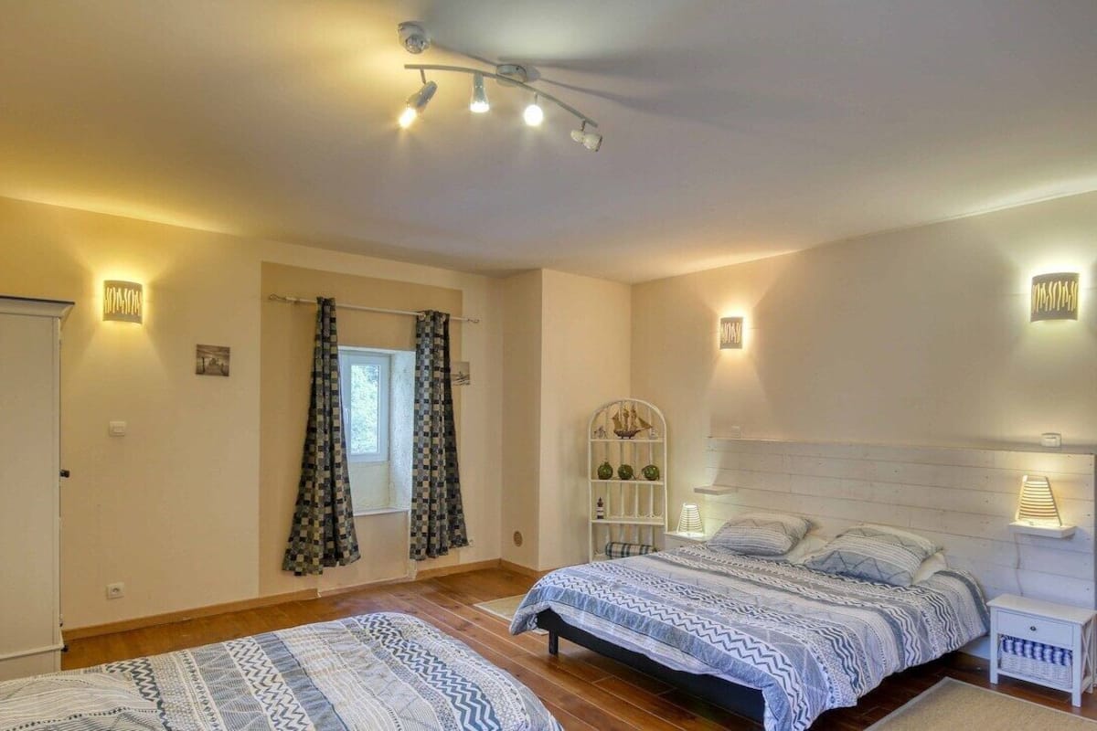 Une chambre avec deux lits, une armoire blanche, une table de chevet et une étagère murale agrémentée d’objets décoratifs.