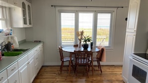 A kitchen with white cabinets, a wooden dining table, and a window with blinds. - Waterfront 3 Bedroom cottage located in beautiful Turkey Point (Vittoria)