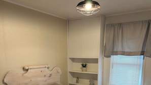 A bedroom with a wooden headboard, a patterned bedspread, a bedside shelf with decorative items, and a window with blinds. - Waterfront 3 Bedroom cottage located in beautiful Turkey Point (Vittoria)