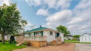 A single-story house with a front porch, a small attached garage, and a paved driveway. - Waterfront 3 Bedroom cottage located in beautiful Turkey Point (Vittoria)