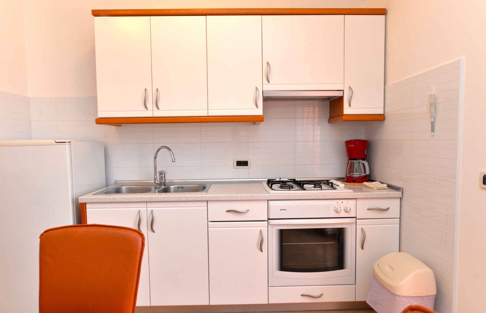 A compact kitchen with white cabinets, a gas stove, a sink, and a red coffee maker.