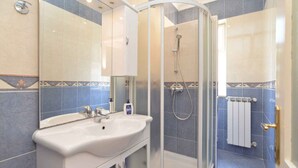 A bathroom with a curved glass shower enclosure, a sink with a mirror, and tiled walls with decorative borders.