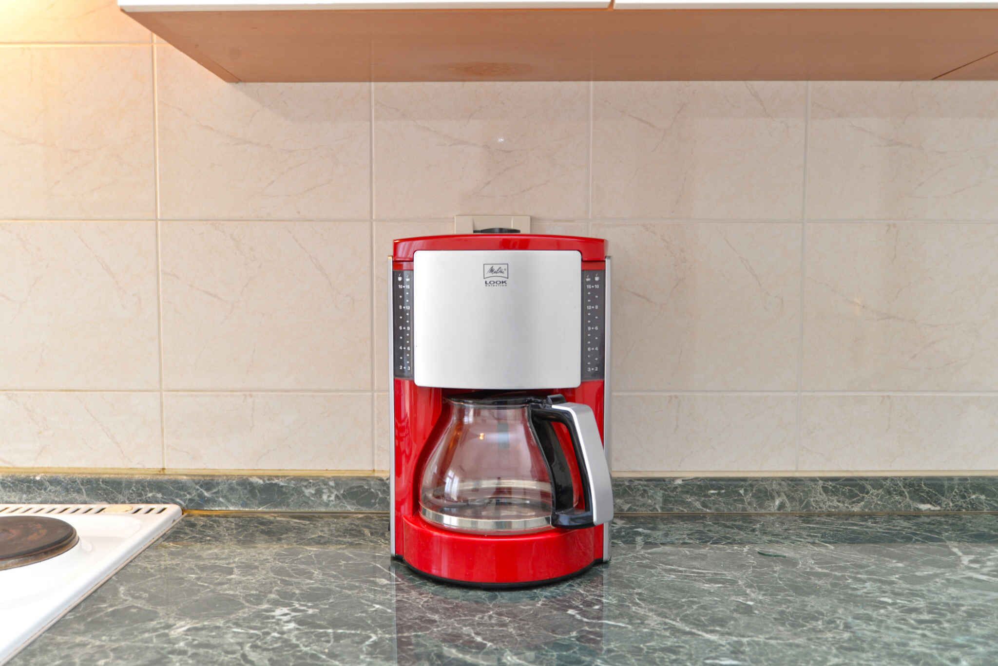 Una cafetera roja y blanca sobre una encimera de mármol.