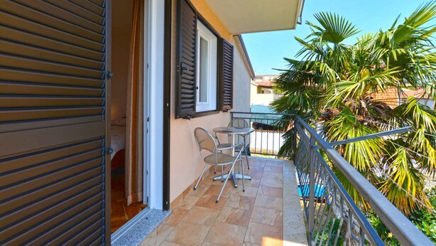 A balcony with a table and chairs, a sliding door, and a view of palm trees.