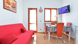 Una habitación con sofá rojo, una mesa de comedor con sillas, un televisor en la pared y una ventana con cortinas.