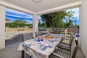 Un espace de restauration extérieur abrité, avec une table dressée pour deux personnes, un mur en pierre et une vue sur le paysage environnant.