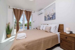 Une chambre à coucher avec un grand lit, une table de chevet avec une lampe, un tableau au mur et une fenêtre avec des rideaux.