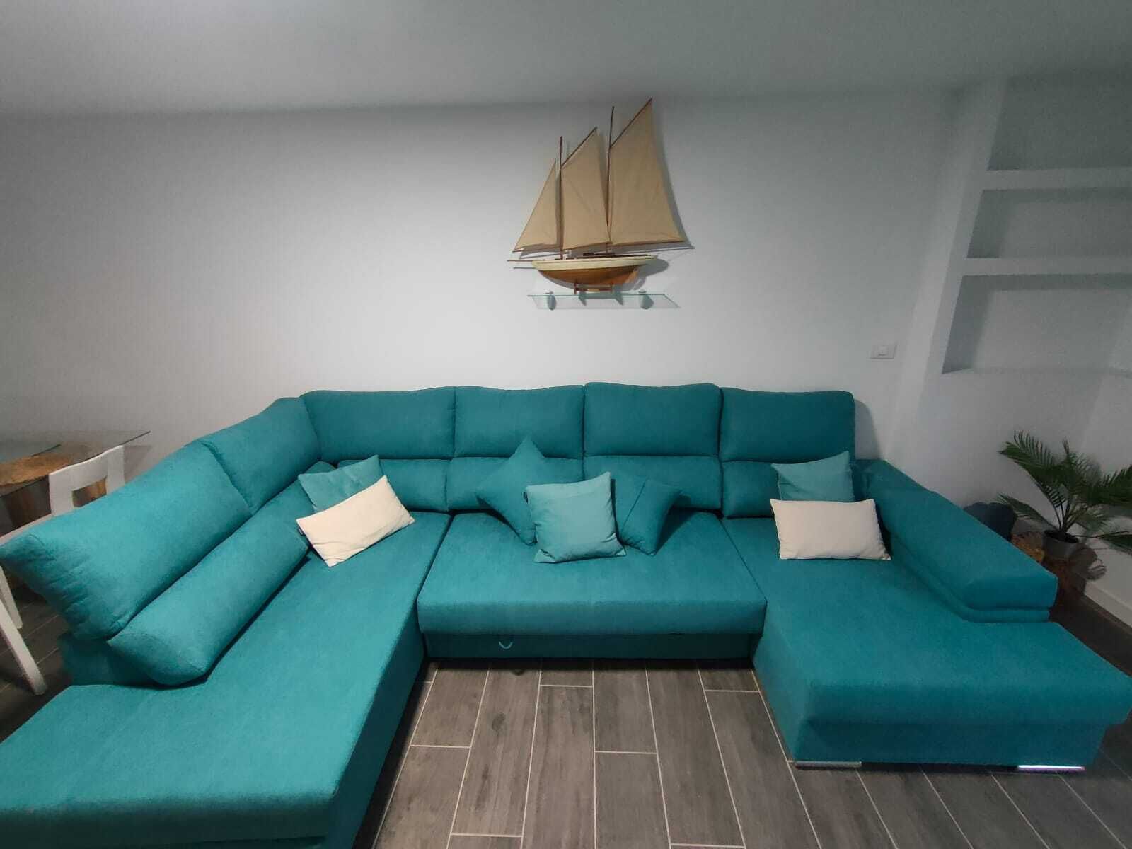 A teal sectional sofa with multiple cushions, a small table, and a potted plant.