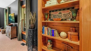 A cozy room with a bookshelf, a sign reading "Farm Fresh Christmas Trees," and a television on a cabinet. - Lush, Private, & Chic Blue Ridge Retreat with 2 Fireplaces- 3 BR - 2.5 BA (Boone)