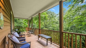 A wooden deck with wicker chairs and a table, overlooking a dense forest. - Lush, Private, & Chic Blue Ridge Retreat with 2 Fireplaces- 3 BR - 2.5 BA (Boone)