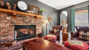 A cozy living room with a brick fireplace, leather furniture, and a view of the outdoors. - Lush, Private, & Chic Blue Ridge Retreat with 2 Fireplaces- 3 BR - 2.5 BA (Boone)