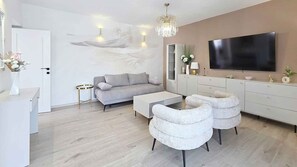 Una sala de estar moderna con un sofá gris, sillones blancos, una mesa de centro, un televisor y una araña.