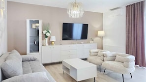 A modern living room with a flat-screen TV, a chandelier, a sofa, a coffee table, and a cabinet.