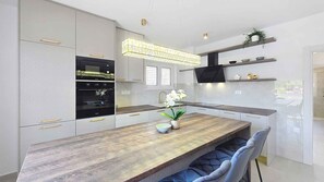 A modern kitchen with built-in appliances, a wooden dining table, and blue upholstered chairs.