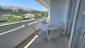 A balcony with a table and chairs, overlooking a mountainous landscape with houses.