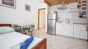 Ein gemütlicher Raum mit Bett, einem kleinen Esstisch, einer Küchenzeile mit Kühlschrank und einem Holzbalken an der Decke.