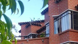 A two-story brick house with a balcony, a gravel driveway, and potted plants. - Suite Gold Rocks Glamping (El Penol)