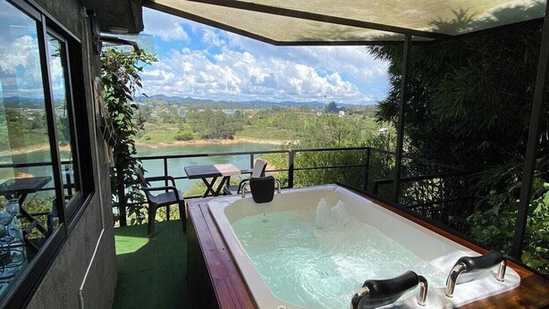A hot tub on a balcony with a view of a lake and mountains. - Suite Gold Rocks Glamping (El Penol)