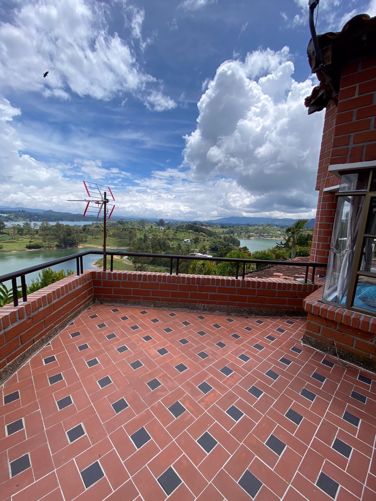 A terrace with a tiled floor, a brick wall, and a view of a lake and hills.