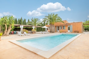 A swimming pool with lounge chairs, a covered seating area, and a building with a stone facade.