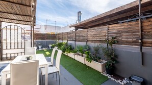 Une terrasse avec une table et des chaises, un petit jardin avec des plantes et une clôture en bois.