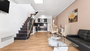 Un salon moderne avec une table basse en verre, un canapé en cuir noir et un escalier menant à la cuisine.
