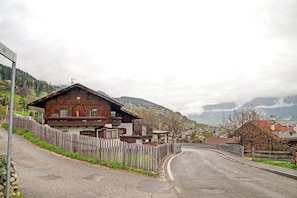 A wooden house with a balcony, a wooden fence, and a curved road.