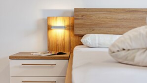 A bedroom with a wooden headboard, a bedside table with drawers, a lamp, and a bed with white bedding. - Apartment 'Klein' with Mountain View, Shared Garden and Wi-Fi (Velturno)